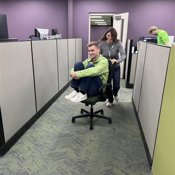 Choice One team members from a civil engineering, surveying, and landscape architecture firm racing through office cubicles during a playful Office Olympics chair‑push event.